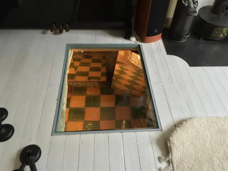 Glasplaat in de houten vloer met zicht op de geruite tegelvloer van de oude kelder in Hoorn