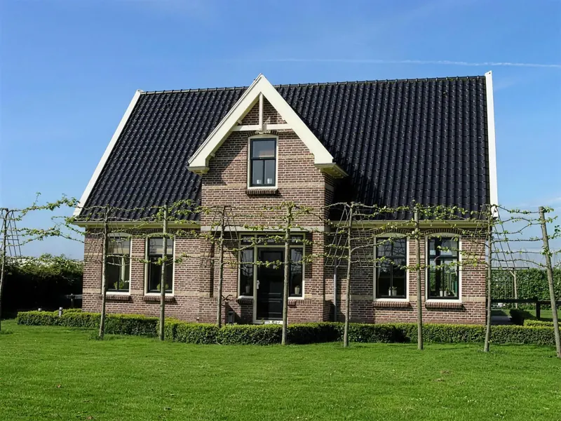 Voorgevel van het woonhuis in Ursem met topgevel boven de voordeur en leibomen ervoor