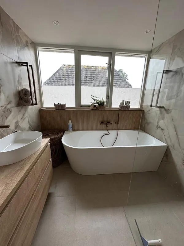 Ligbad onder drie ramen tegen een geribbelde wand, koperkleurige kraan, badkamer in Opmeer