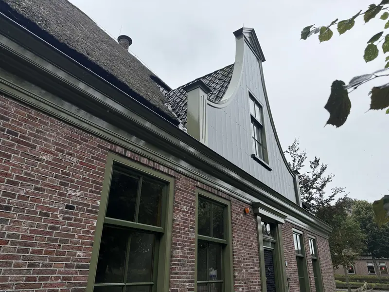 Gebogen topgevel met lichtgrijze verticale delen boven de bakstenen voorgevel, stolpboerderij in Opmeer