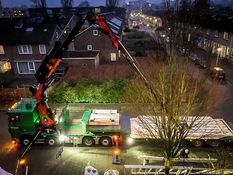 Kraanwagen en dieplader met elementen voor de dakopbouw in een woonstraat in Amsterdam, avond