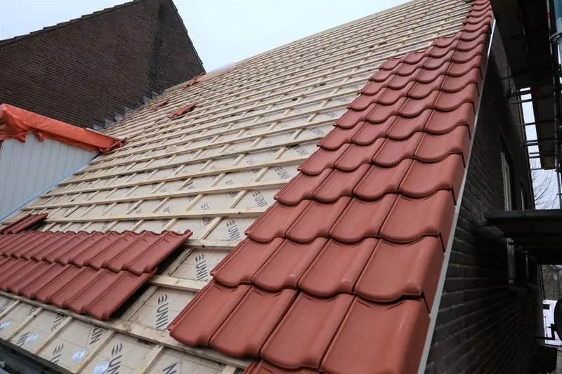 Nieuwe rode dakpannen op panlatten en isolatieplaten tijdens de dakrenovatie in Obdam