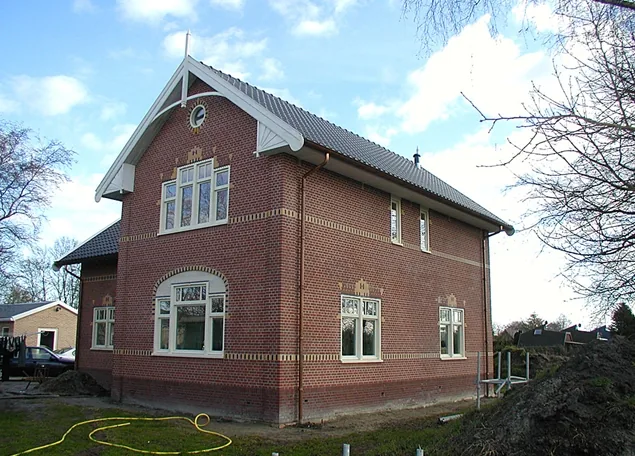 Zij- en topgevel van het woonhuis in Opmeer met witte makelaar, rond venster en gele sierbanden