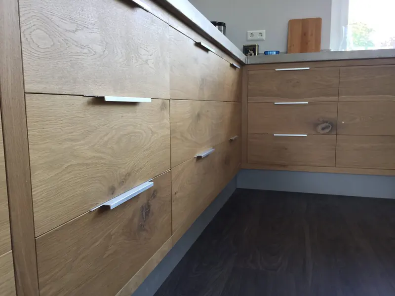 Eiken keukenlades met knoesten en aluminium greeplijsten onder een betonnen werkblad