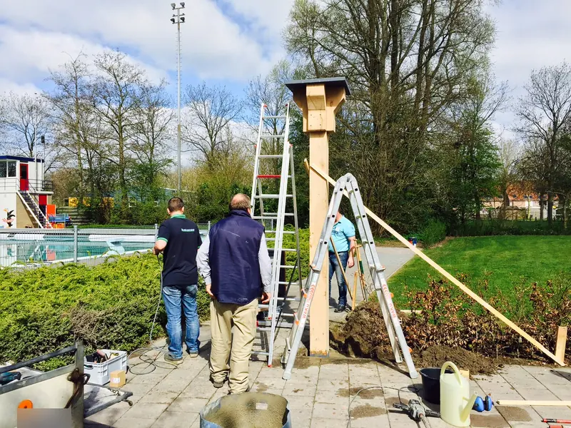 Houten paal voor de klok wordt gesteld bij zwembad 't Woudmeer, met ladders en schoren