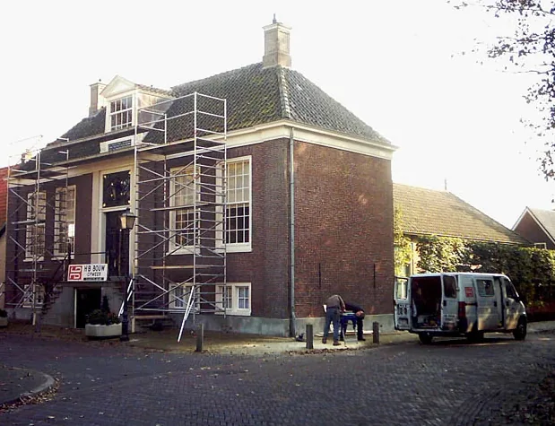 Raadhuis in Hoogwoud in de steigers, met bouwbord van HB Bouw en een bedrijfsbus voor de deur