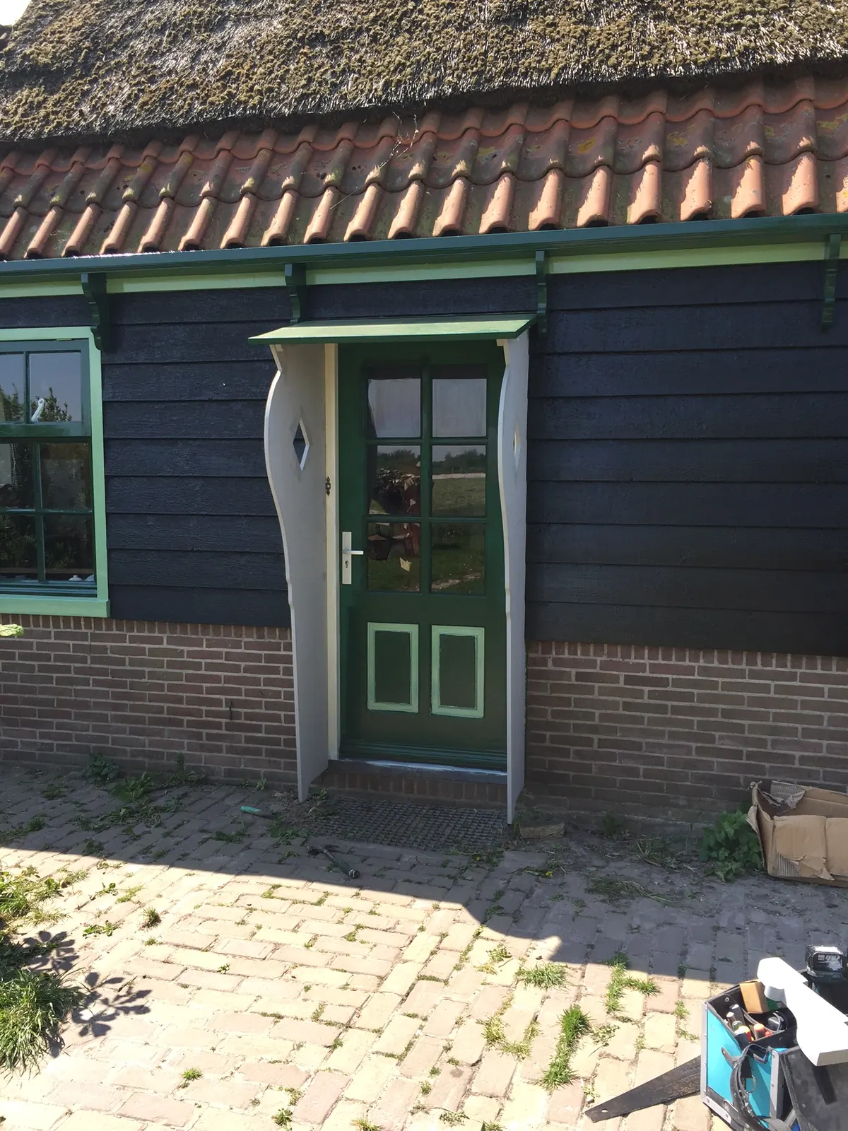 Groene deur tussen gebogen lichtgrijze zijwangen onder een klein afdak in de donkere houten wand van een molen