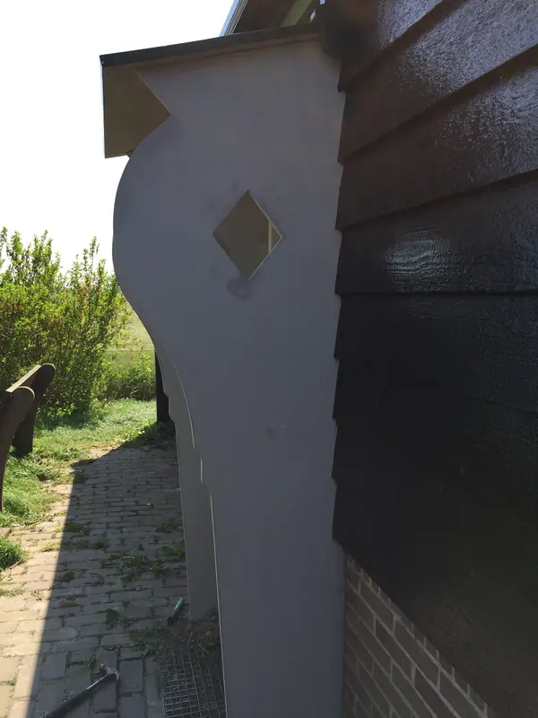 Gebogen zijwang met ruitvormige uitsparing naast de donkere houten wand van een molen