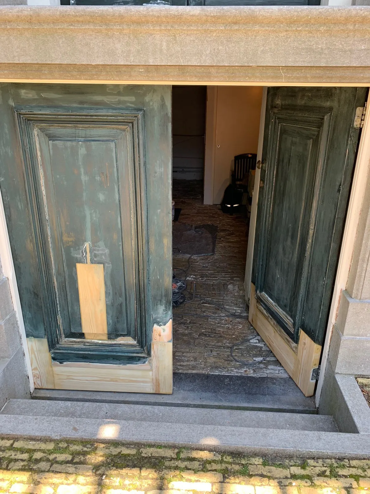 Dubbele paneeldeur met nieuw hout aan de onderkant in de stenen ingang van het raadhuis in Hoogwoud