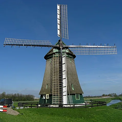 Molen bij Obdam met riet gedekt lijf, groene onderbouw en wieken tegen een blauwe lucht