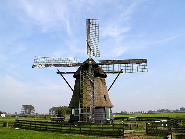 Molen Westerveer met riet gedekt lijf, schoren en houten hek in het weiland