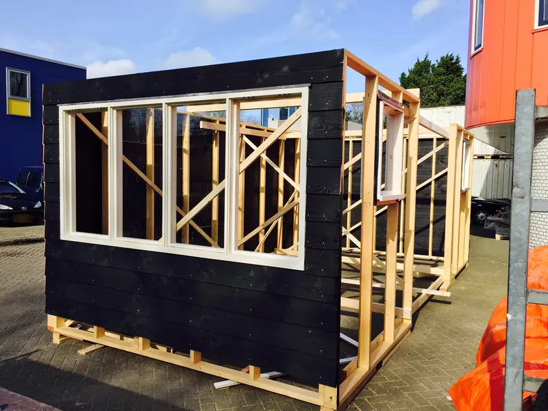 Schuurwand met zwarte houten bekleding en wit kozijn, achter de wand het houten skelet