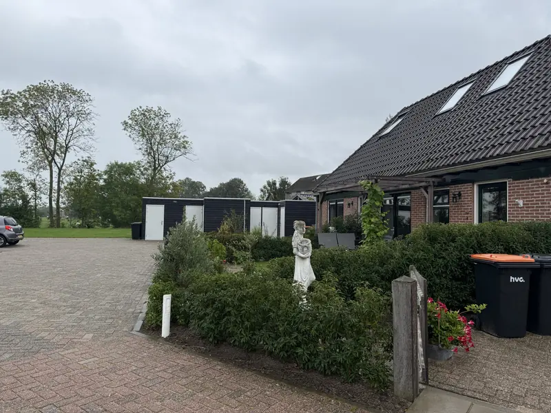 Bergingen van zwarte delen met witte deuren achter het voormalige café, naast een vleugel met dakramen