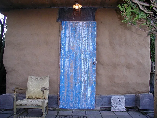 Oude blauwe deur in een lemen wand op een voet van hout, met een lamp erboven