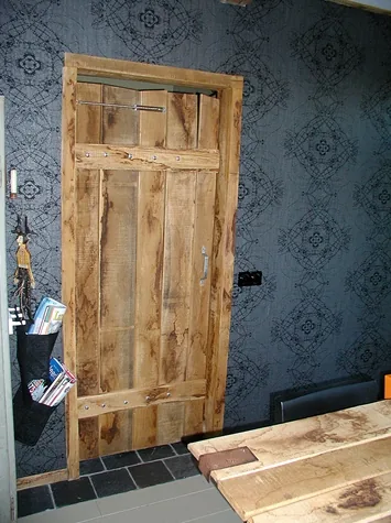Deur van ruwe houten planken in een ruw houten kozijn tegen donker behang