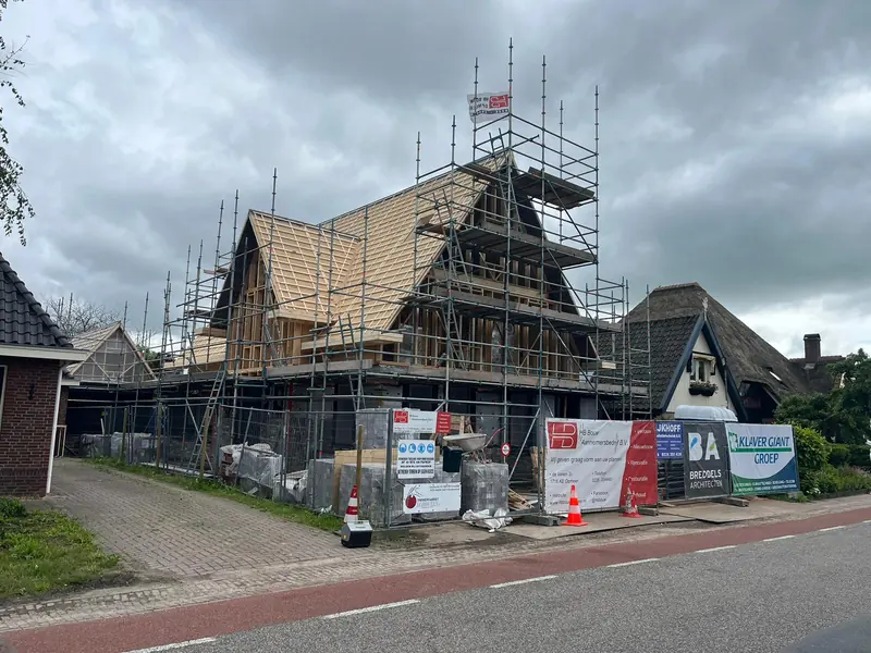 Ruwbouw van het woonhuis in Obdam in de steigers, met houten dakelementen en bouwborden aan de straat