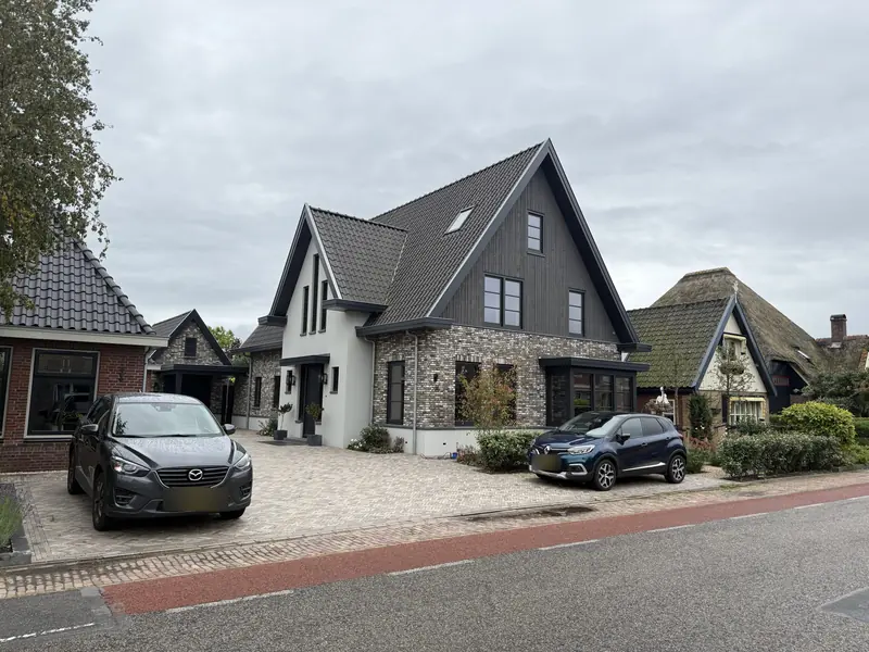 Voorgevel van het woonhuis in Obdam met grijze baksteen, wit stucwerk en houten topgevel aan de straat