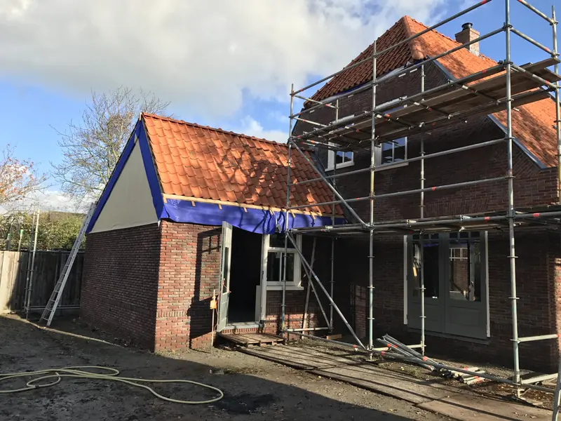 Woonhuis in Spanbroek met oranje pannen in de steigers en een aanbouw met dakfolie, tijdens de afbouw